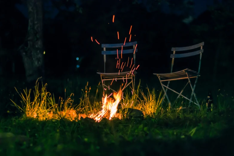 two empty chairs sitting in the grass by the fire