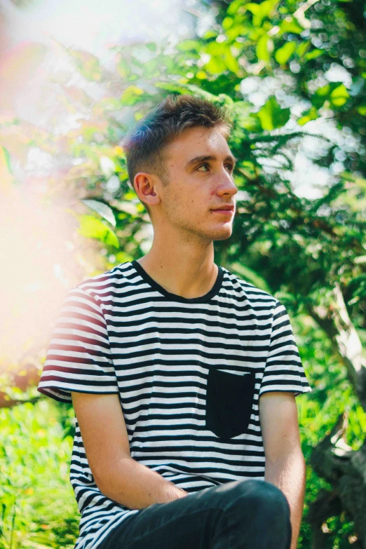 young man wearing stripes sits and looks into distance