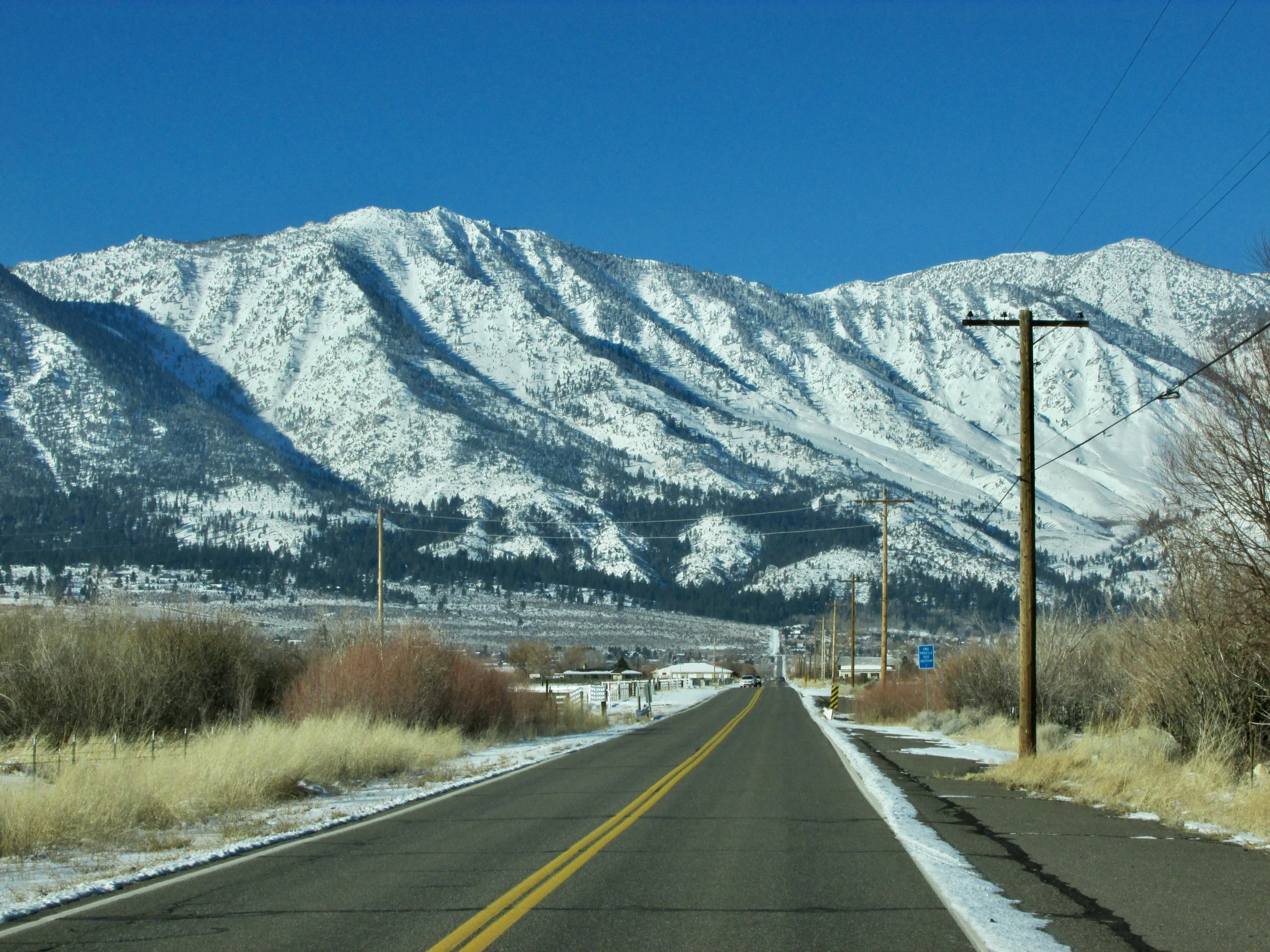 the mountains are covered with snow as a street sign stands in front of it