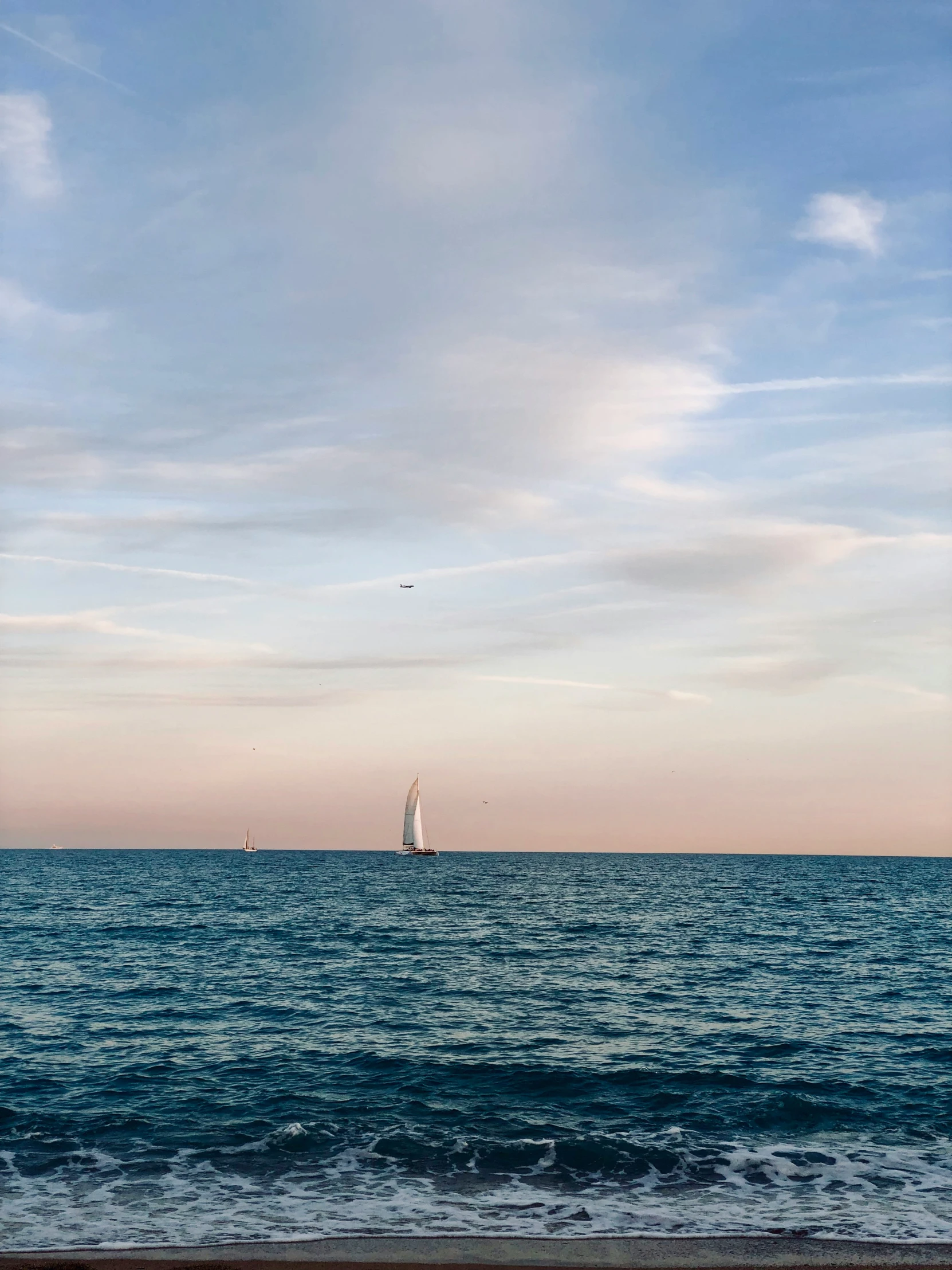 a sailboat is on the water in a pink sky