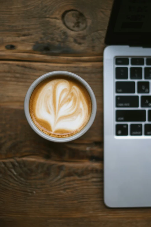 a cup of cappuccino sitting next to an open laptop