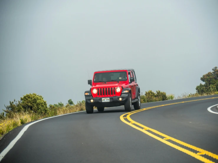 a red jeep drives down a rural road