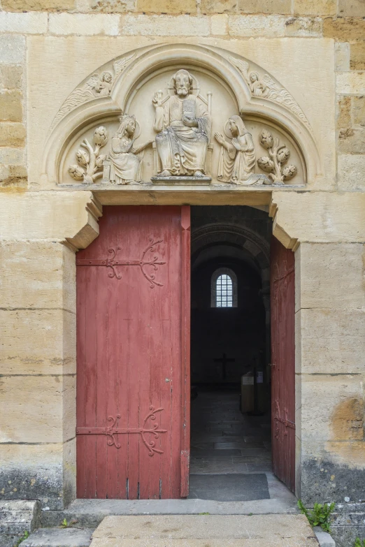 a stone doorway with two red doors and a statue above it