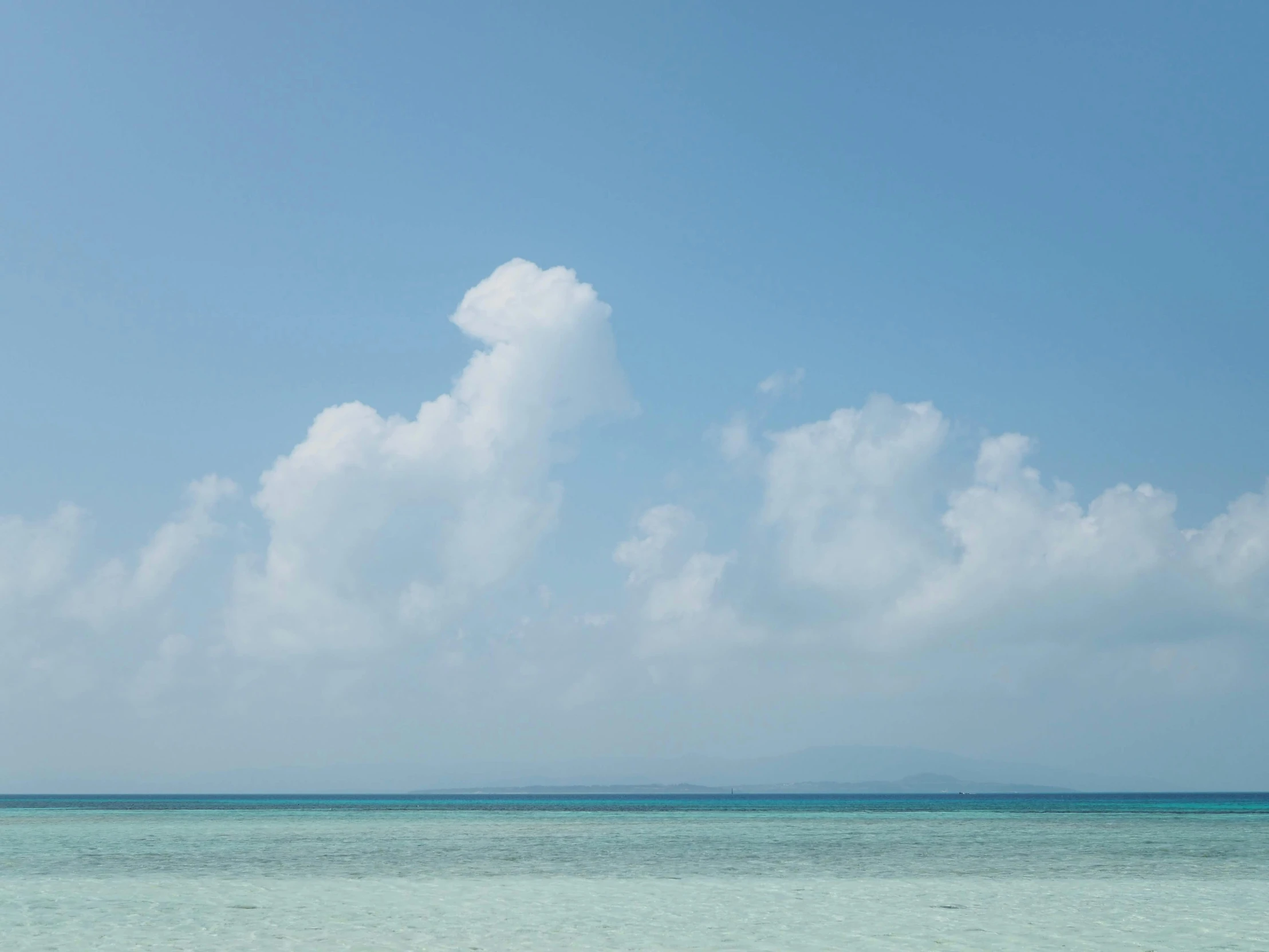 a blue sky with white clouds is seen above an ocean and a boat on the water