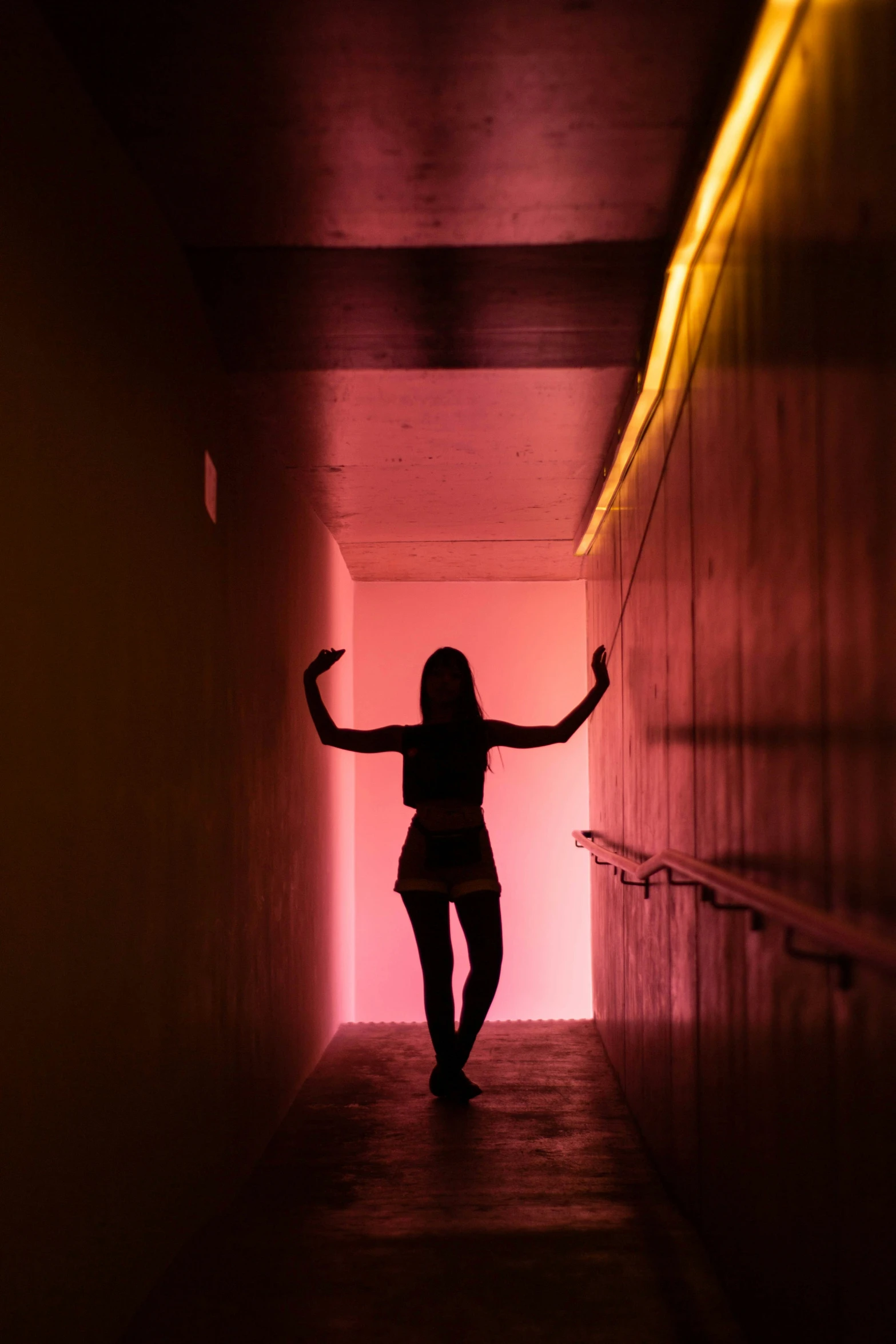 a woman standing alone in a long dark hallway