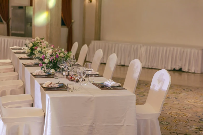 a table set with all white chair covers and flowers