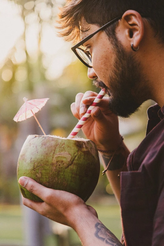 a man wearing glasses drinking from a coconut