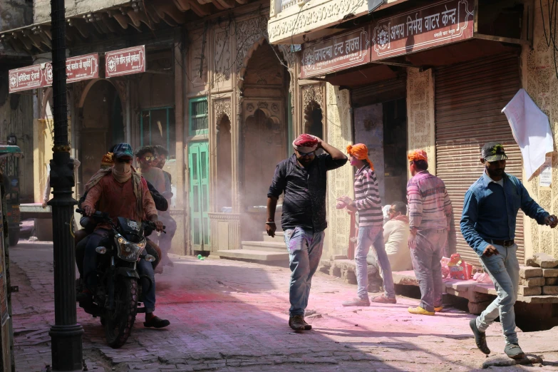 four men are walking down a street and another one is sitting on a motorbike