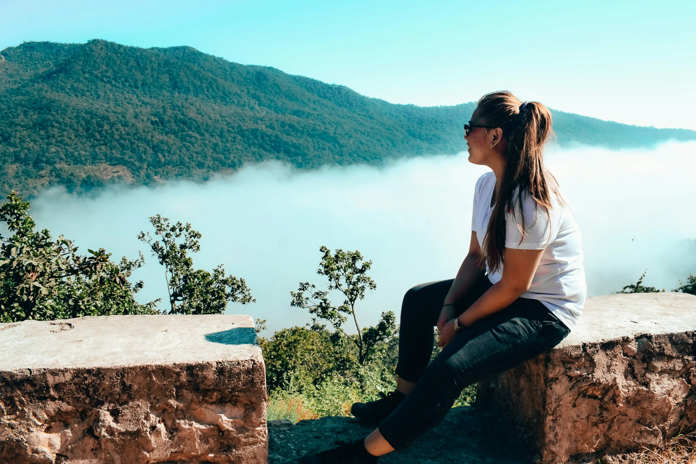 a woman sitting on top of a stone wall