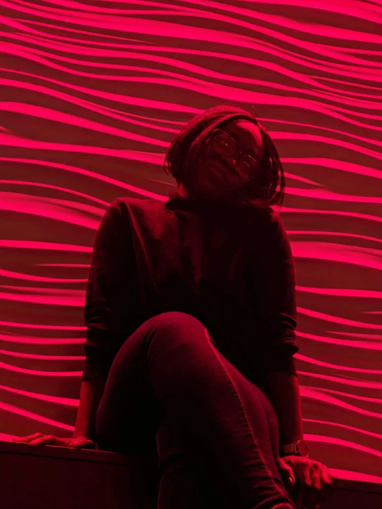 a woman sitting on a bench against a wall with a bright red light