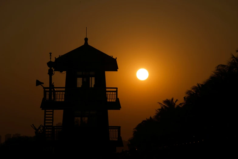 the sun sets over a lighthouse with the silhouette of the building in front