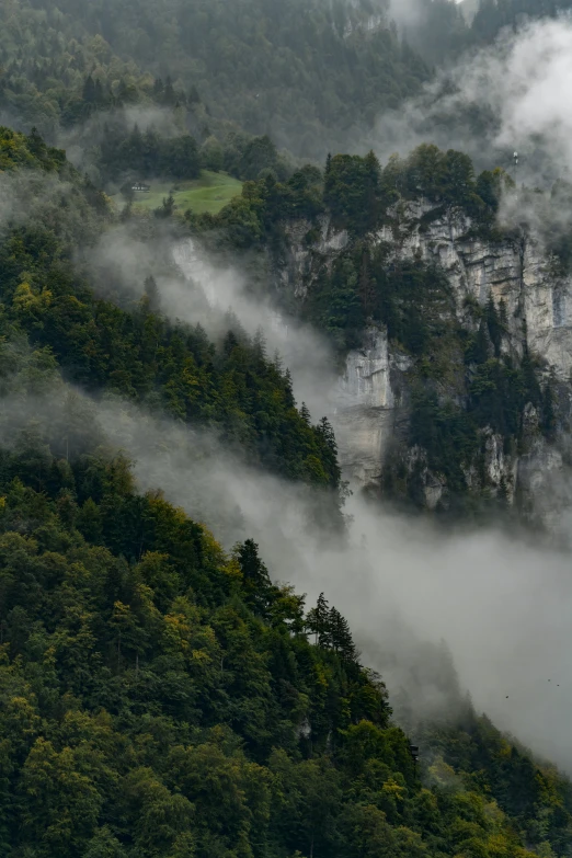 some clouds covering trees and mountains under a cloudy sky