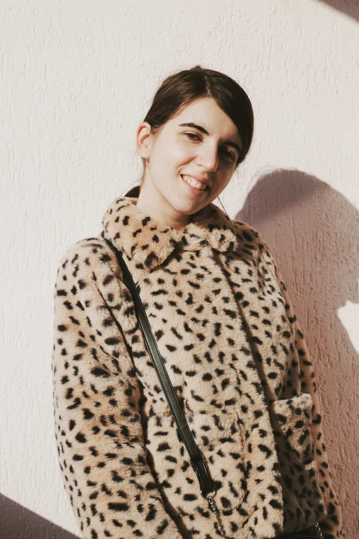 a woman poses in front of a wall with her purse