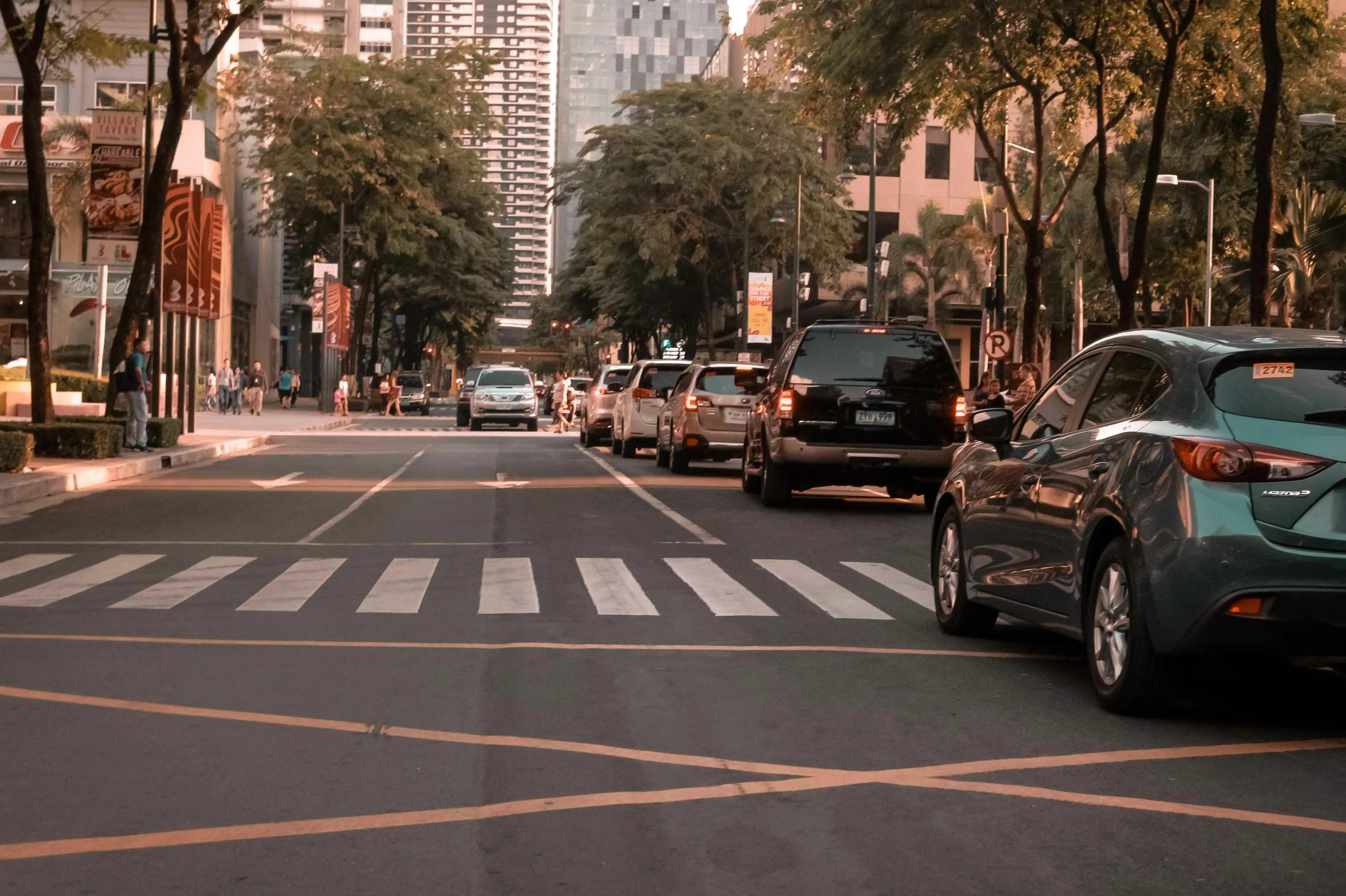 a city street with cars parked and crosswalks and buildings on either side