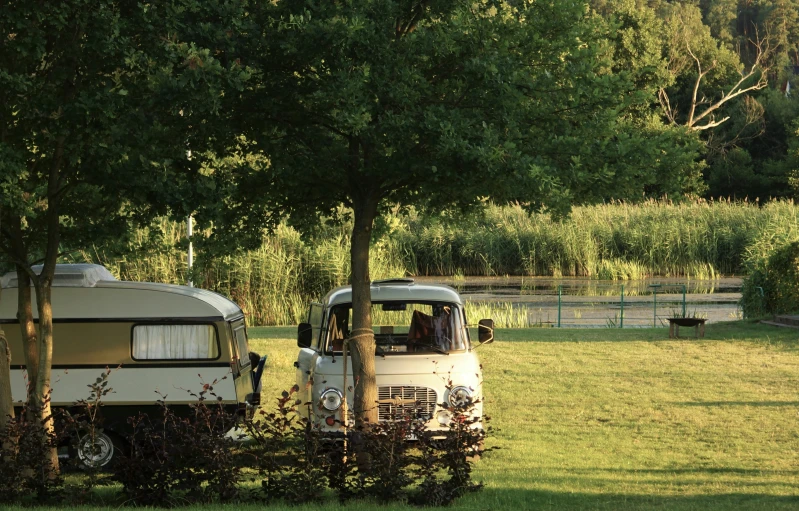 an older truck towing a trailer behind a fence and some trees