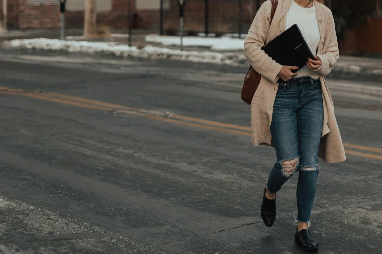 a woman walking across a street wearing ripped jeans and a white top