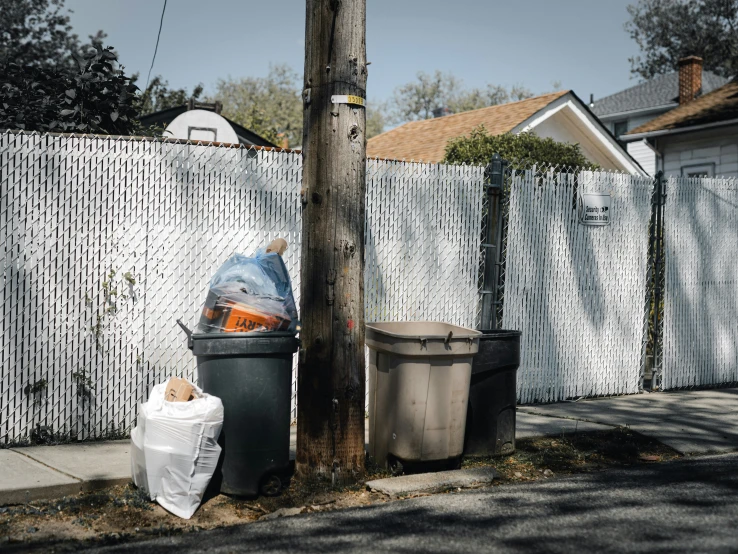 trash cans and garbage bags line the sidewalk behind a fence