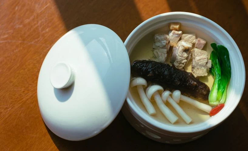 a plastic container containing soup and meat sitting on top of a wooden table