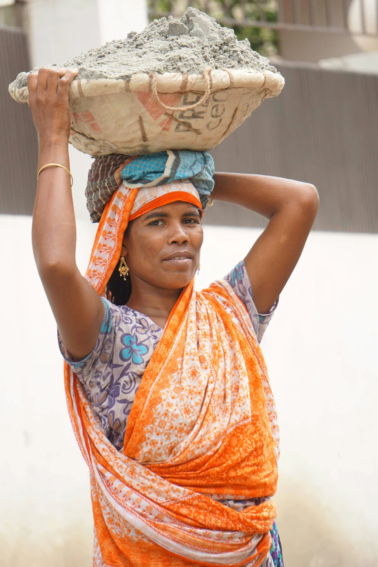 woman wearing orange scarf carrying large bowl on head