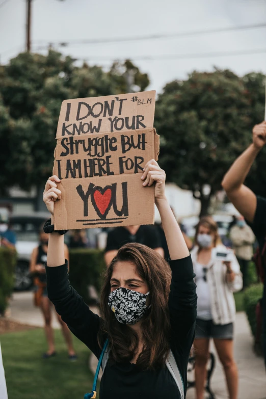 a woman holding a cardboard sign with the message i don't know your struggle but where for you