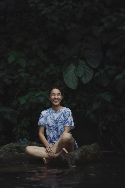 smiling woman sitting in water next to lush green tree