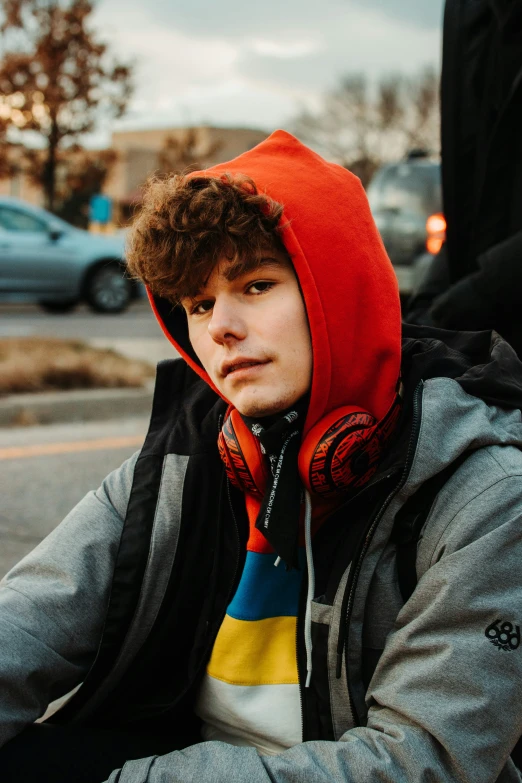 a young man wearing a red hoodie is sitting on the street