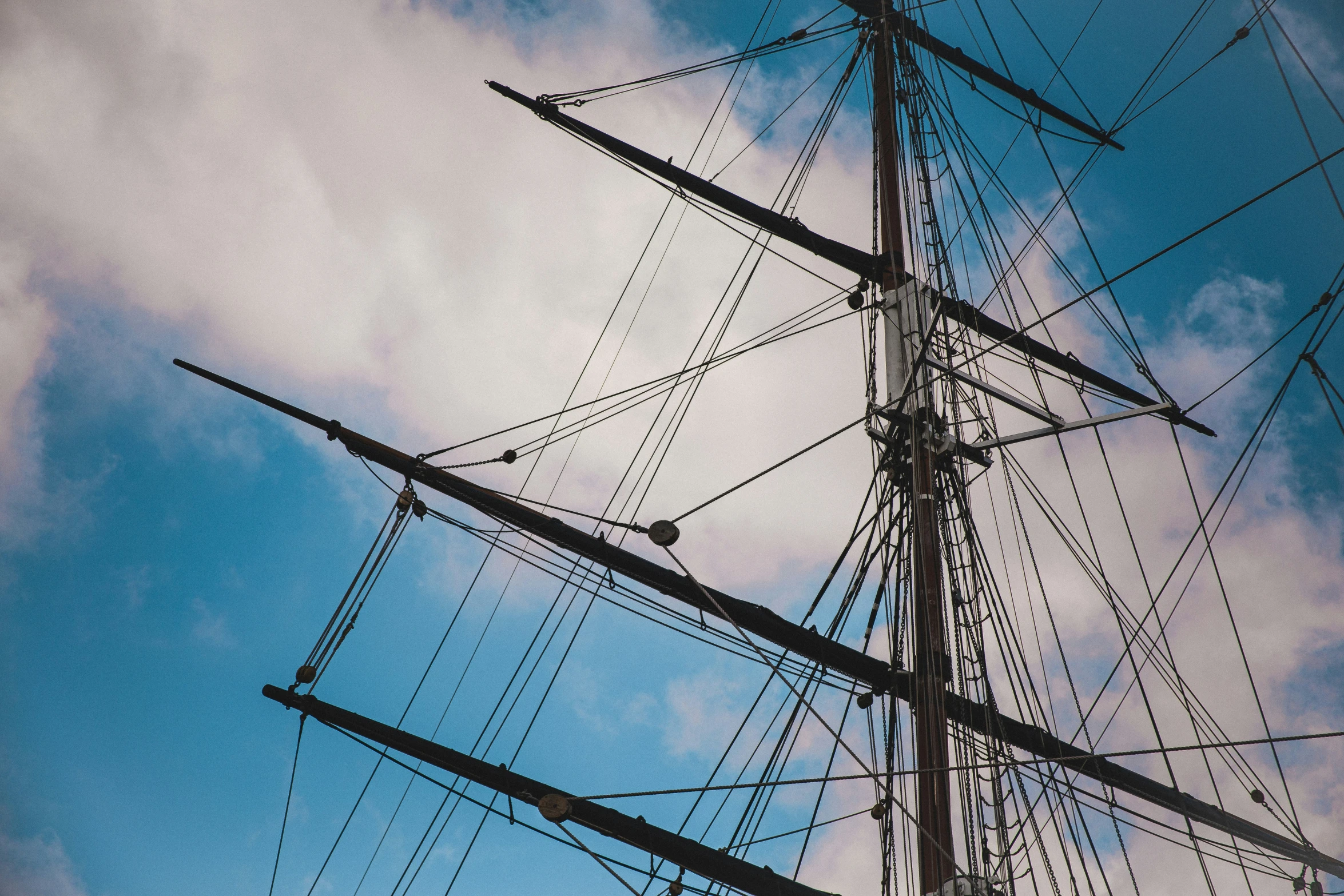 the rig of a sail boat is against a blue sky with clouds