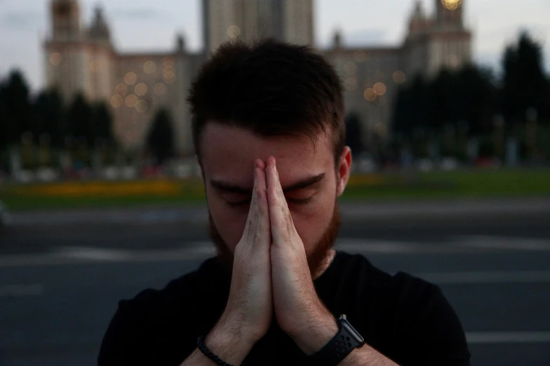 a man covers his face in front of a city tower