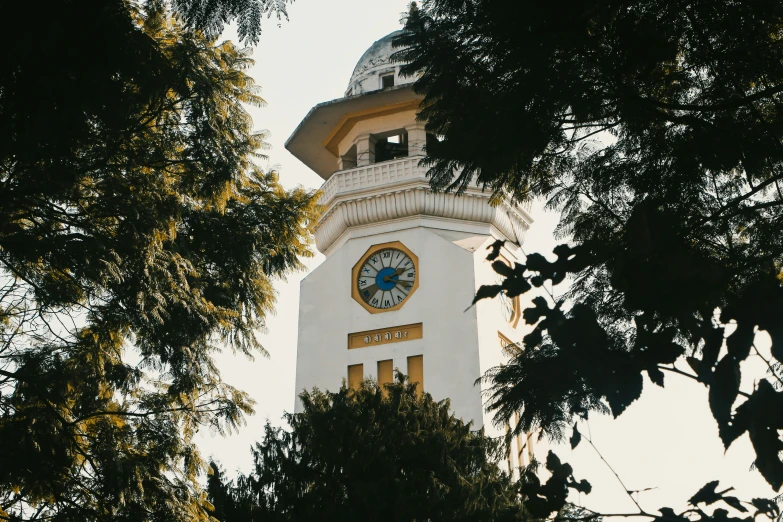 a white clock tower has a gold and blue clock on it's face