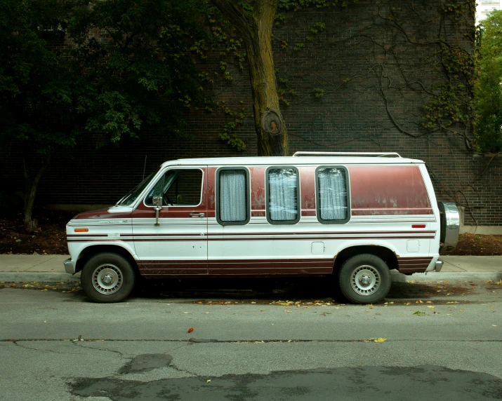 an old maroon and white van parked on the side of the road