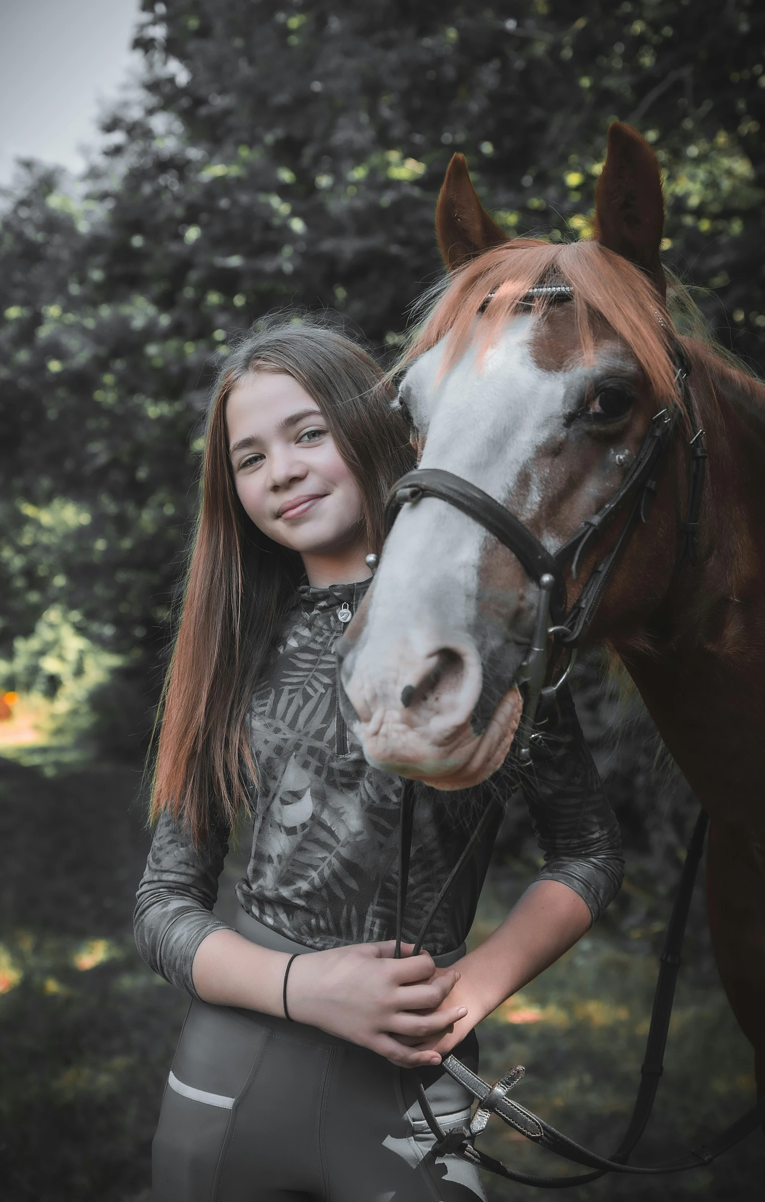 a girl standing beside a brown horse and trees