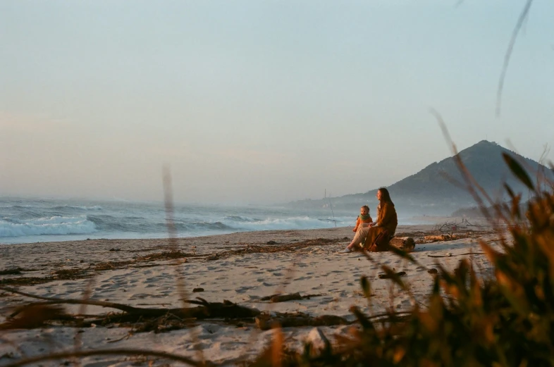 two people sit on the sand as the waves crash