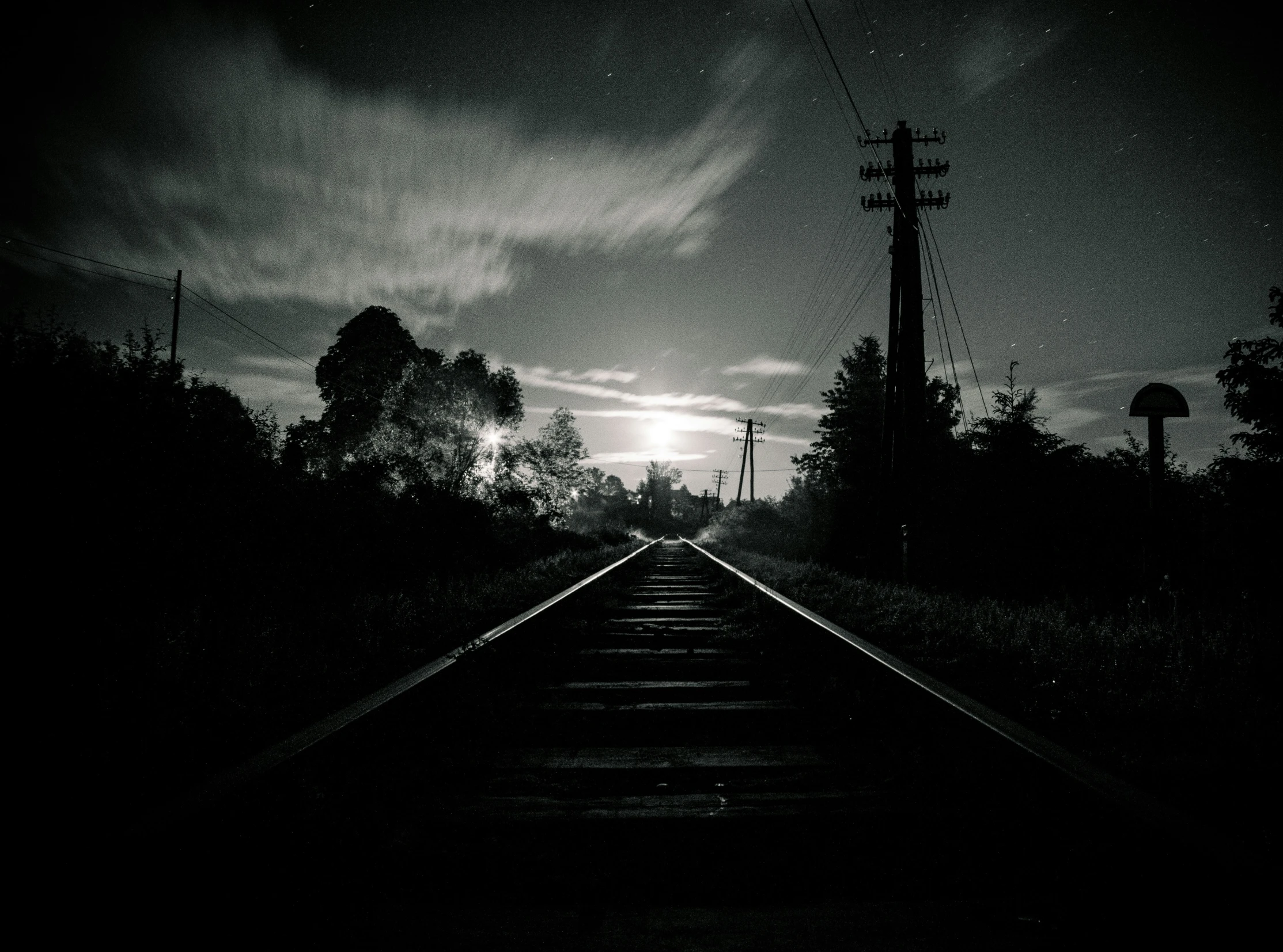 black and white pograph of a railroad track with a moon in the distance