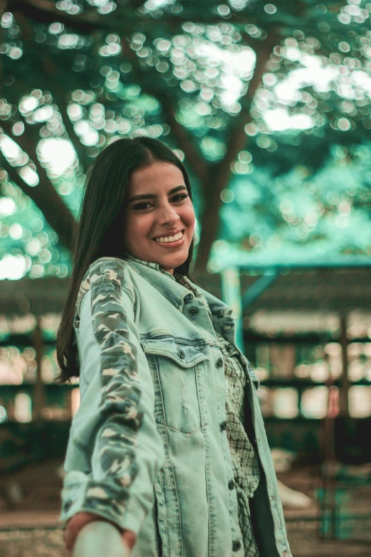 the smiling woman holds her arms in front of trees