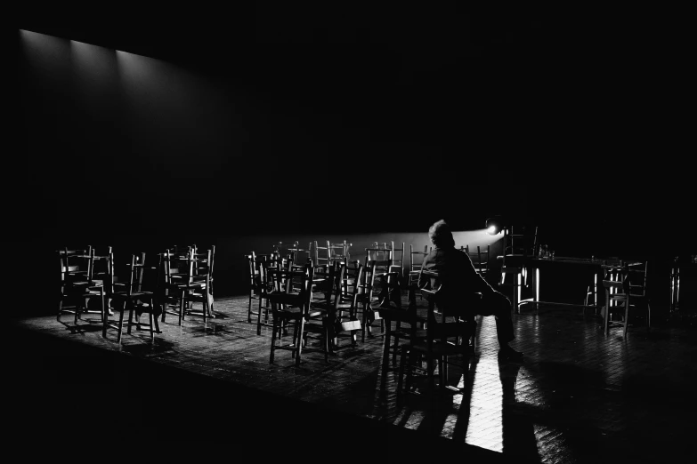 empty chairs sit in the dark as a conductor stands with his arm extended