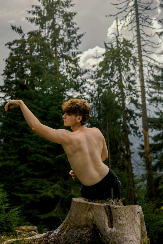 a shirtless boy flying a frisbee above a forest