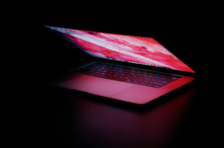 a red laptop with an iphone logo is illuminated in the dark