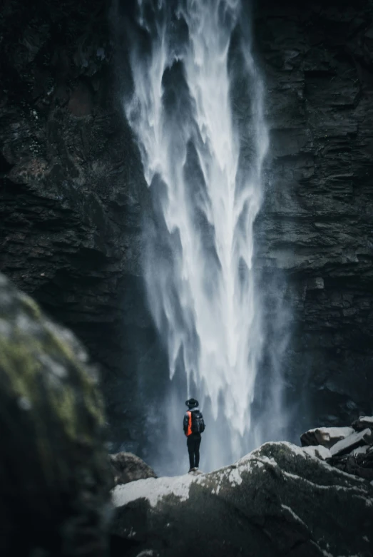 man standing at the base of a large waterfall