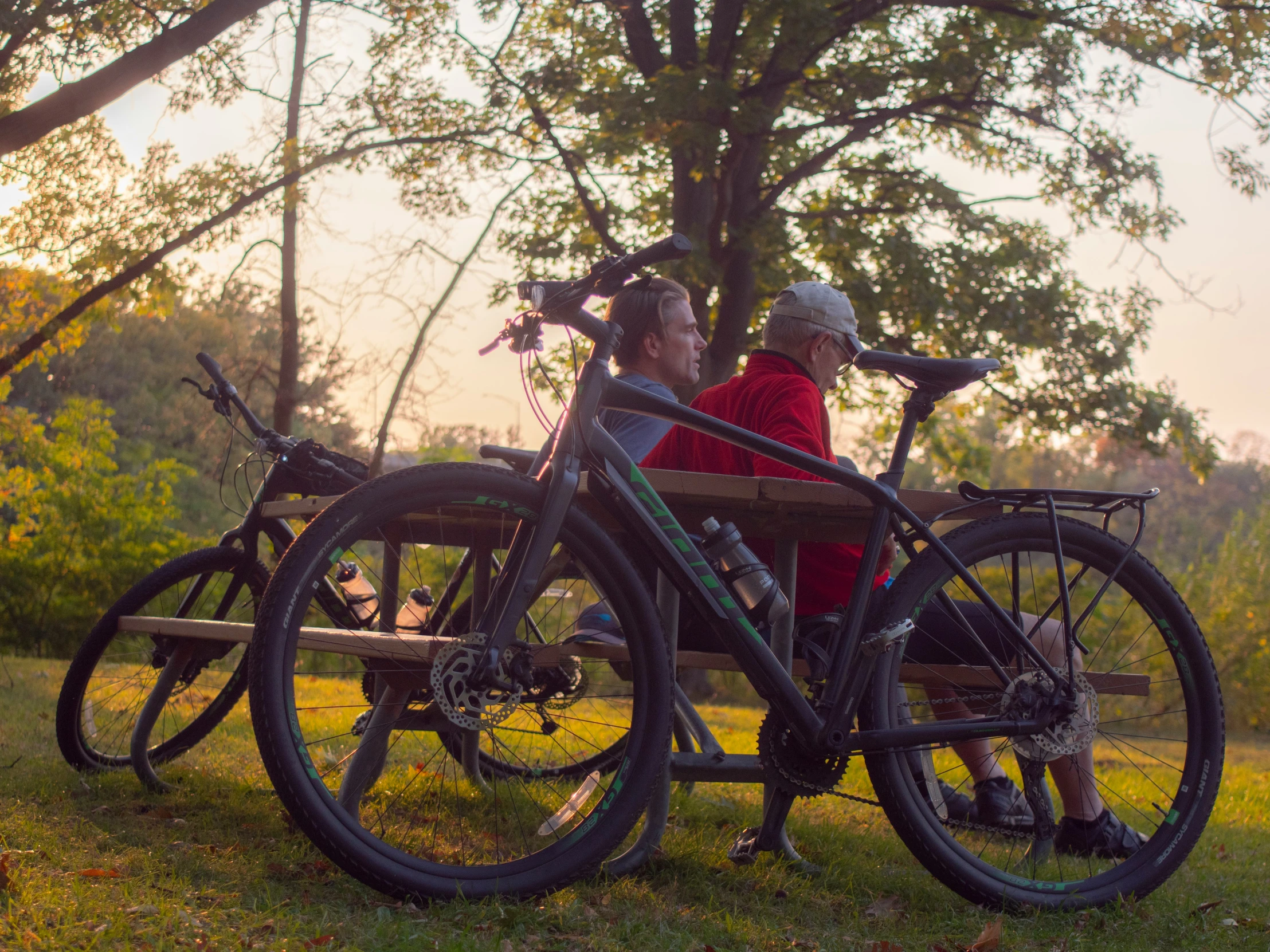 two people sitting at a park bench on bikes