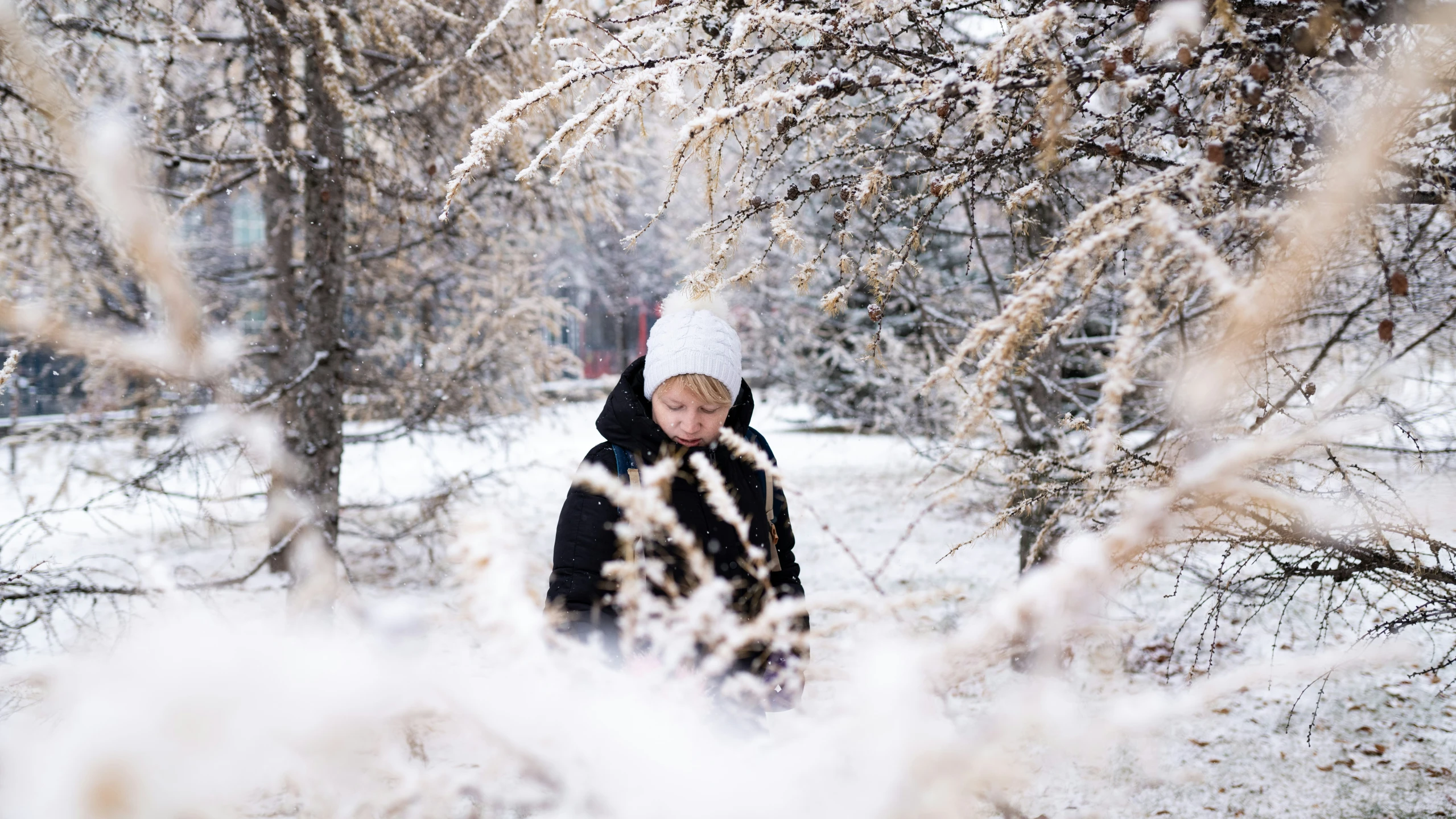 the man in a hat is walking through the snow covered woods