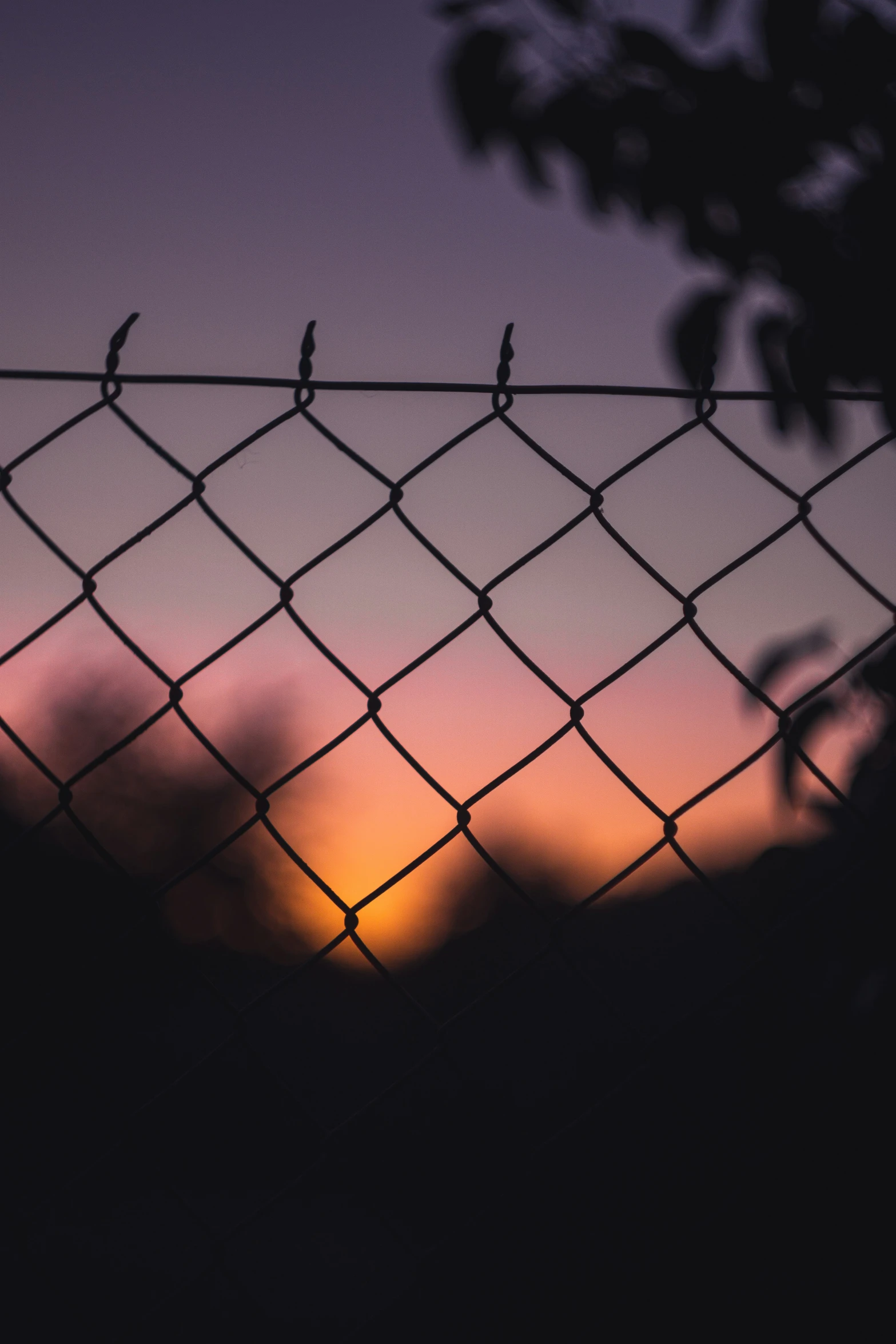 the sun is going down behind a chain link fence