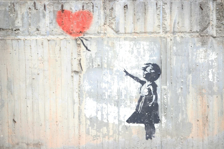 a child holding a red heart balloon on a cement wall