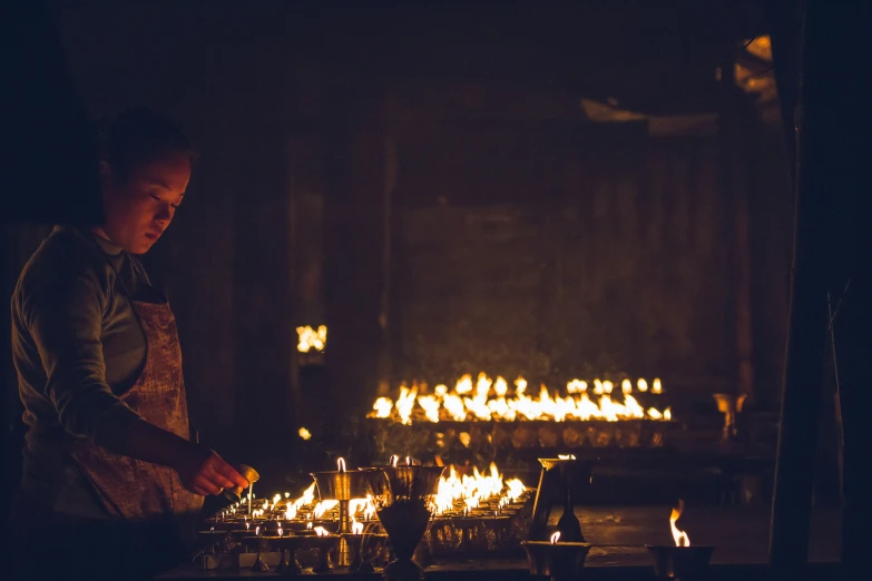 the woman in the apron is working on a large table full of lit candles