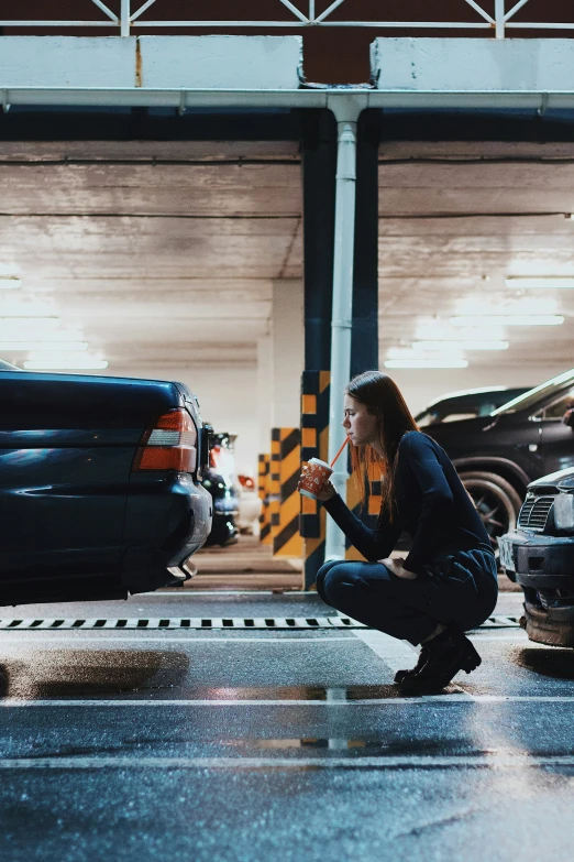 a woman sitting on a ramp smoking in front of cars