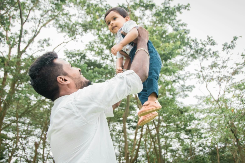 a man holds up his son as he walks through the woods