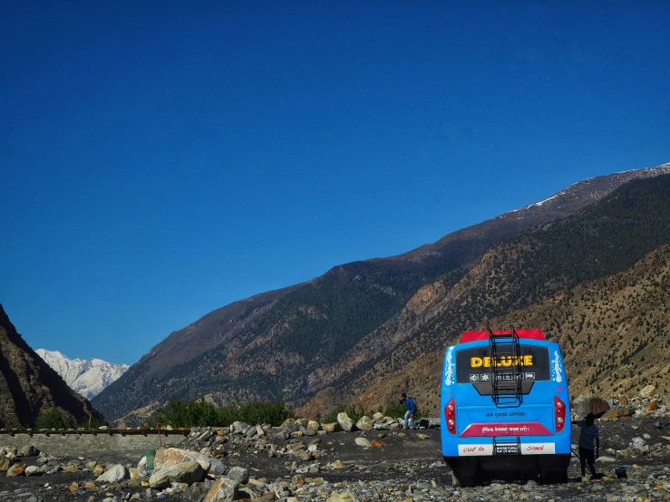 a blue bus parked at a bus stop in a mountainside