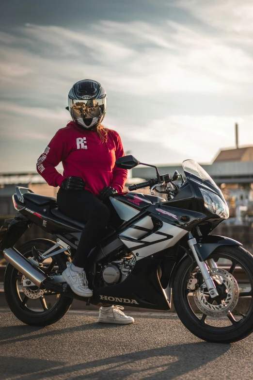 a young person sitting on a motorcycle with an open helmet