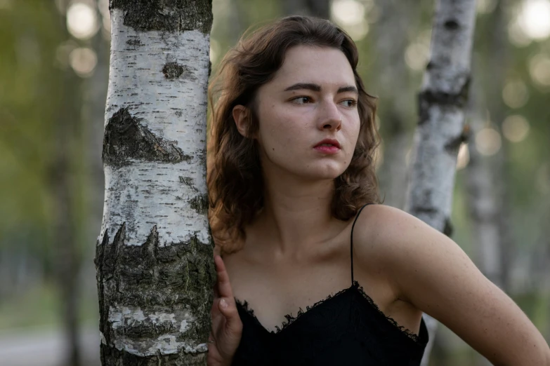 the woman is standing near the tree posing for the camera