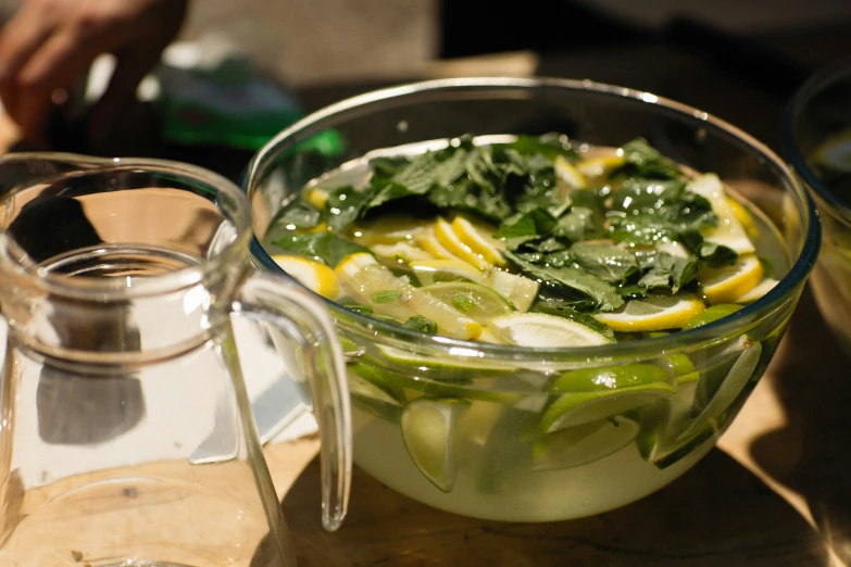 a glass bowl filled with green vegetables and slices of lemon