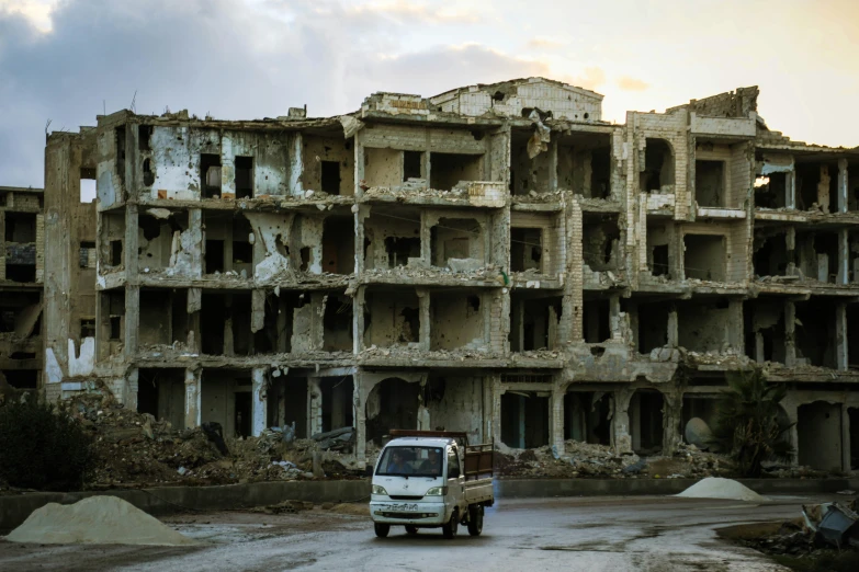 a small truck sits on the road in front of a burned building